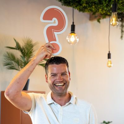 Lachende man houdt rood vraagteken boven zijn hoofd.
