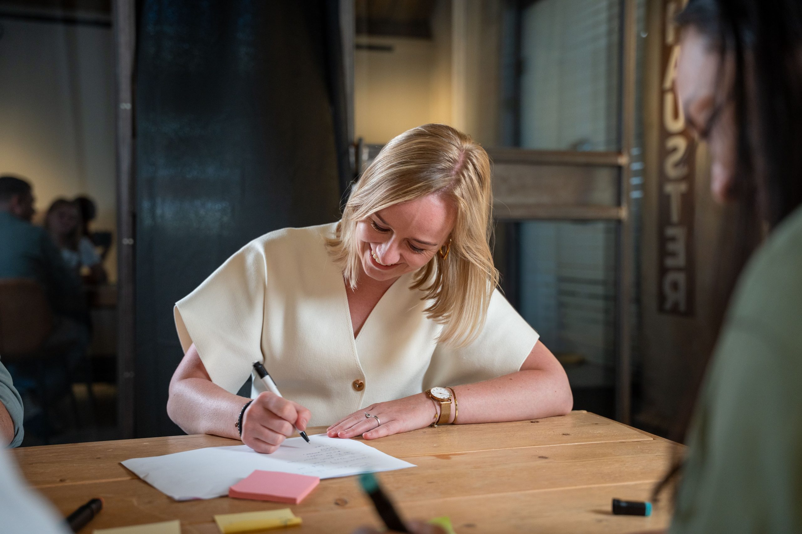 Vrouw schrijft lachend aantekeningen tijdens een creatieve sessie.