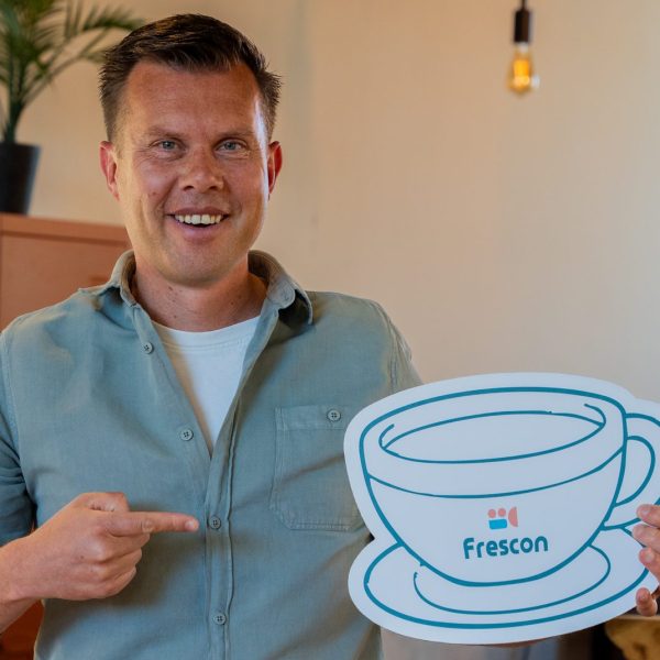 Man houdt koffiekop-icoon vast met Frescon-logo.