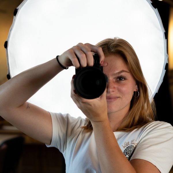 Fotograaf richt camera naar voren met softbox op de achtergrond.