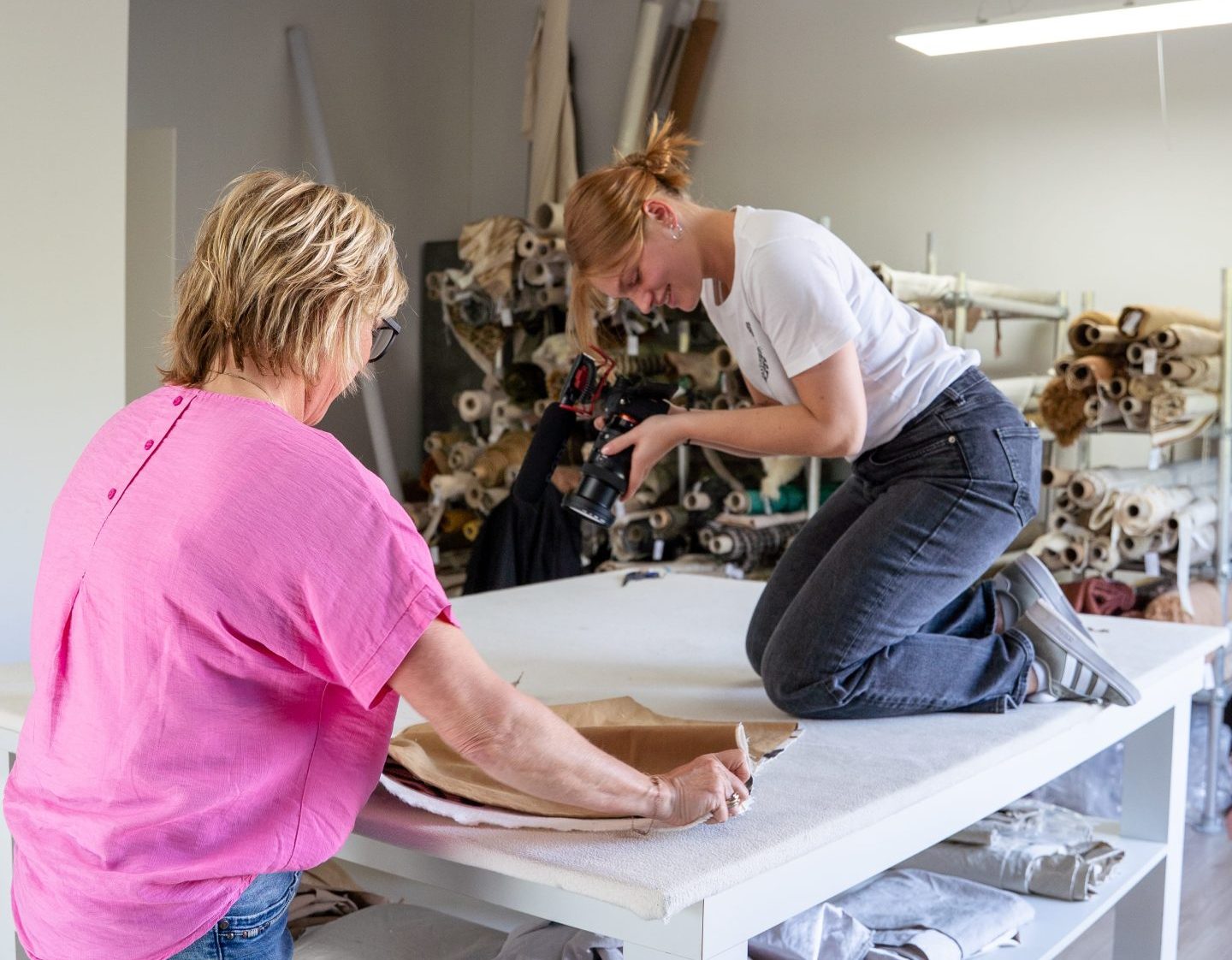 Vrouw fotografeert terwijl collega met stof werkt in een atelier.